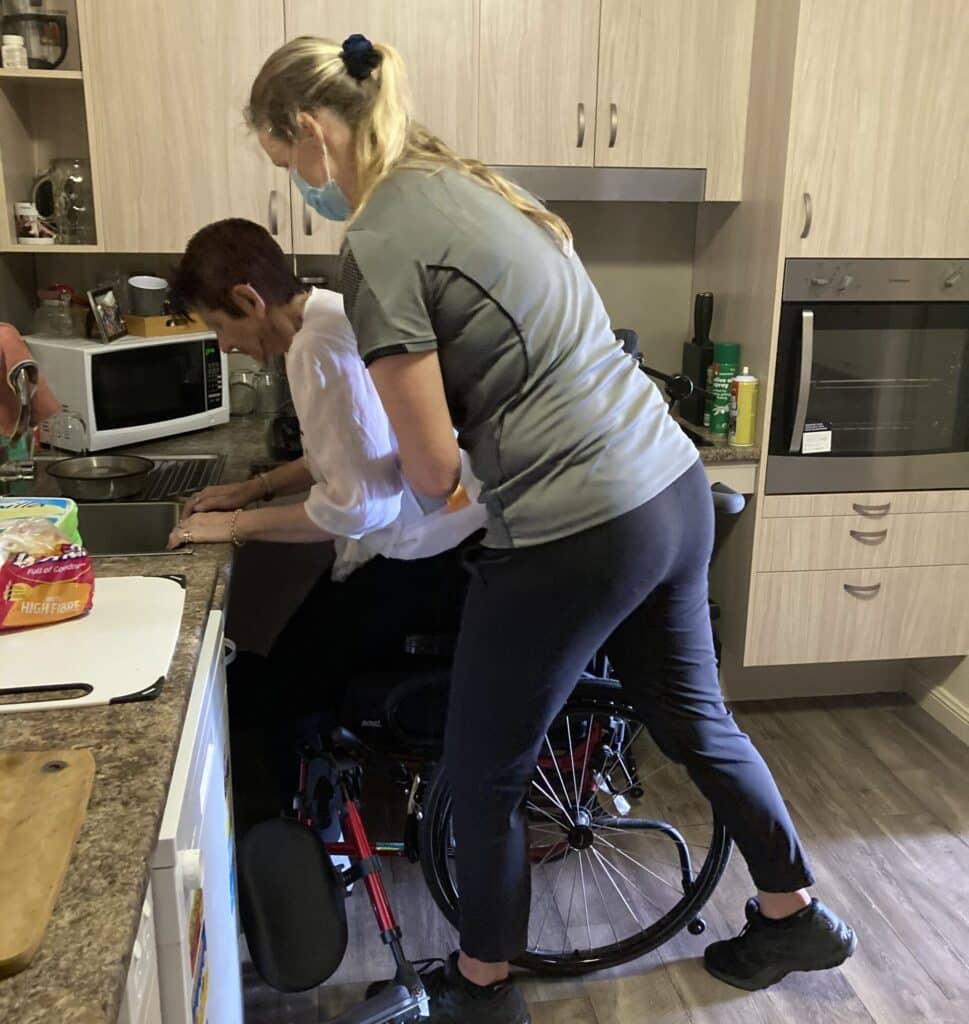 Mobile Physio helping a NDIS client to stand up out of her wheelchari